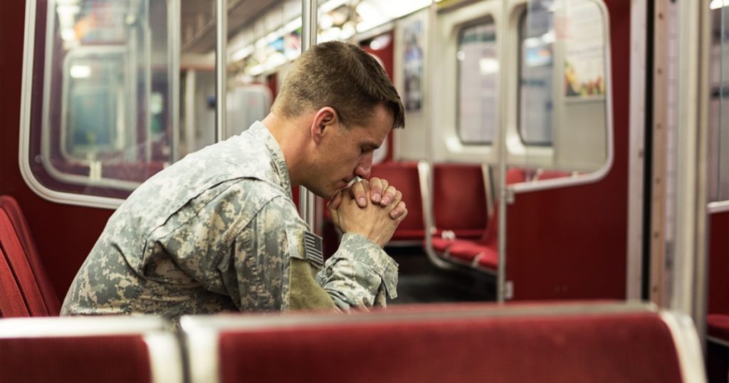 Soldier Sitting Alone in Train Car with Hands Clasped Together & Eyes Closed