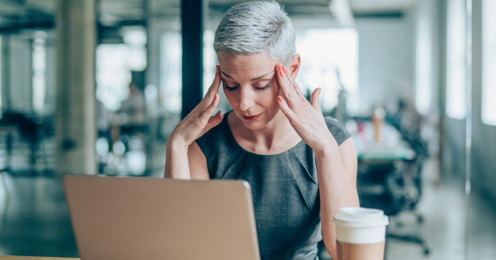 Professional Woman Sitting at Computer with Hands on Head with Headache